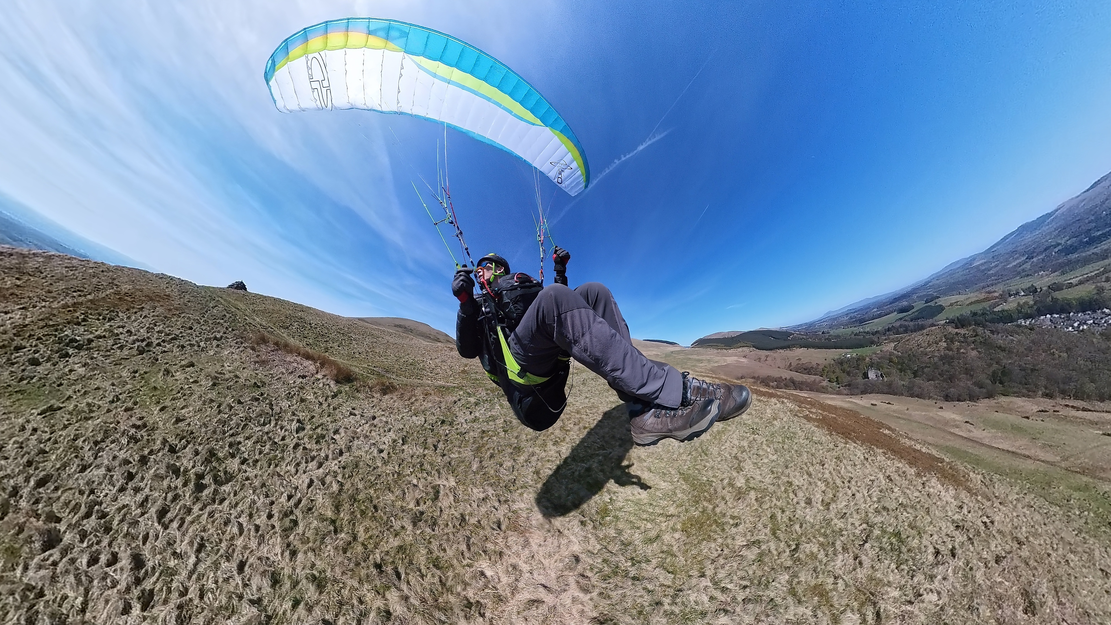 A paraglider skimming low over a Scottish hillside.